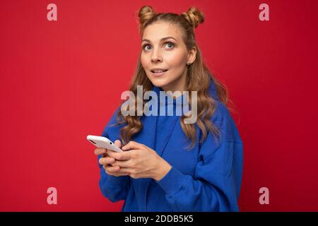Bild einer denkenden träumenden jungen schönen Frau posiert isoliert über rote Wand Hintergrund mit Handy. Stockfoto