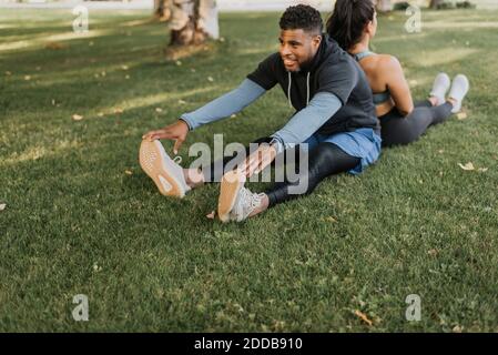 Mann berührt die Zehen, während er sich mit der Frau Rücken an Rücken sitzt Im Hinterhof Stockfoto