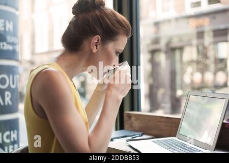Junge Frau trinkt Kaffee, während mit Laptop im Café Stockfoto