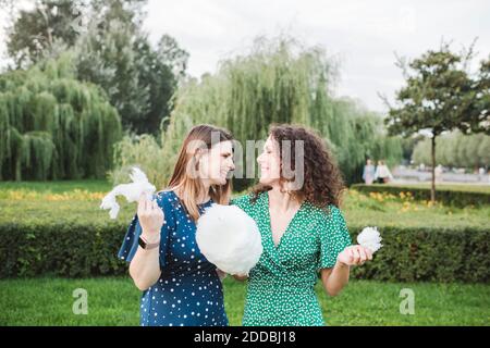 Lächelnde Freundinnen essen große Zuckerwatte im Park Stockfoto