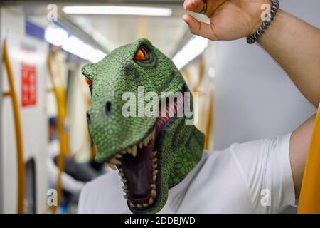 Männlich trägt Dinosaurier-Maske während der Reise im Zug Stockfoto