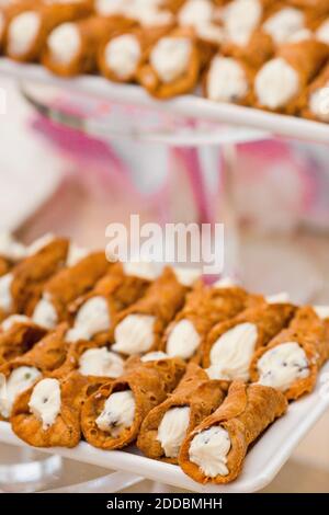 Kleine Cannoli gestapelt auf weißen Keramikschalen bei einem Catering-Event. Vertikale Farbfotografie mit geringer Schärfentiefe Stockfoto