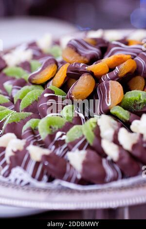 Mit Schokolade überzogene Orangen- und Kiwi-Fruchtbonbons. Bonbons mit Milch und weißer Schokolade auf dem Tablett im Bankettsaal. Stockfoto