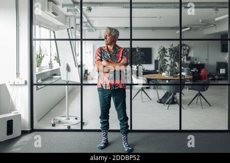 Geschäftsmann in ungezwungener Atmosphäre mit gekreuzten Armen an der Glaswand Im Büro Stockfoto