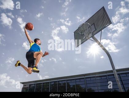 Junger männlicher Athlet, der beim Basketballspielen Ball in den Reifen schmiss An sonnigen Tag Stockfoto