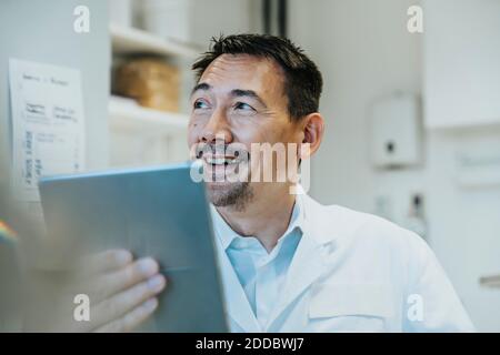 Lächelnder Wissenschaftler mit digitalem Tablet, während er im Labor sitzt Stockfoto