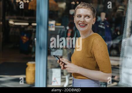 Glückliche Frau hält Smartphone wegschauen, während im Stehen Stadt Stockfoto