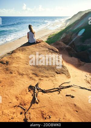 Frau sitzt auf Felsformation, während Blick auf das Meer während Sonniger Tag Stockfoto