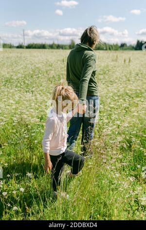 Mutter hält die Hand der Tochter beim Gehen auf der Wiese Stockfoto