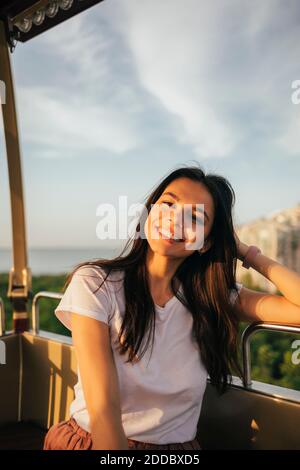 Lächelnd schöne junge Frau sitzt mit der Hand im Haar genießen Fahrt mit dem Riesenrad Stockfoto