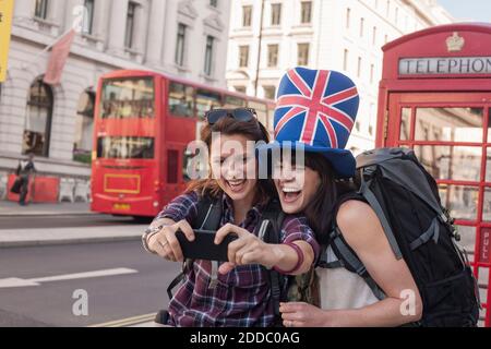 Glückliche Frau, die Selfie mit einem Freund macht, der einen Hut mit britischer Flagge trägt Gegen rote Telefondose in der Stadt Stockfoto