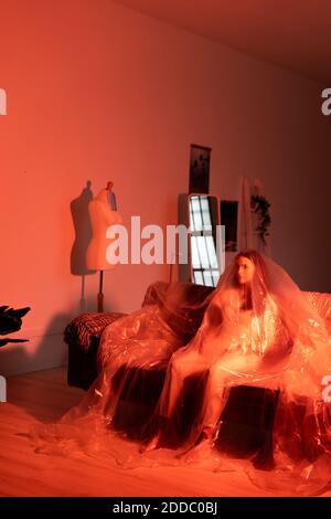 Besorgt junge Frau in Kunststoff auf dem Sofa sitzen bedeckt Zuhause während der COVID-19 Stockfoto