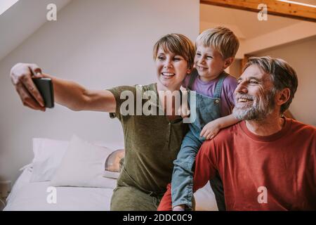 Glückliche Mutter, die Selfie auf dem Smartphone während Vater und Sohn sitzt neben zu Hause Stockfoto