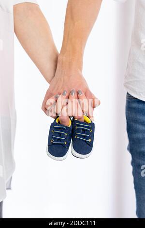 Nahaufnahme Bild von glücklichen Paar der schwangeren Mutter mit Vater hält Hände kleine Schuhe. Paar Hände halten Baby Jungen Schuhe Stockfoto