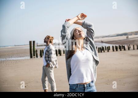 Junge Frau mit geschlossenen Augen und aufgehobenen Armen Strand an sonnigen Tagen Stockfoto