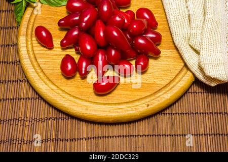 Stillleben - frische große Dogwood Beeren, lila Pflaumen und ein Zweig Basilikum auf einem Holzbrett, aus der Nähe Stockfoto