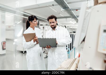 Eine Wissenschaftlerin, die im Labor einen Kollegen mit einem Laptop ansieht Stockfoto