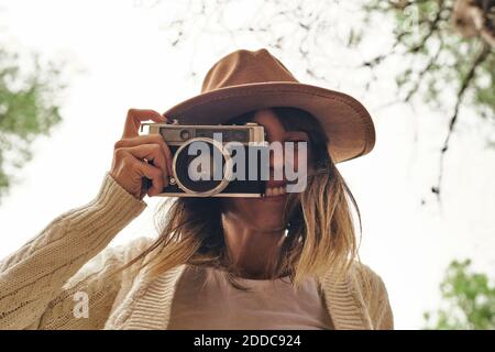 Lächelnde Frau, die im Wald durch die Vintage-Kamera fotografiert Stockfoto
