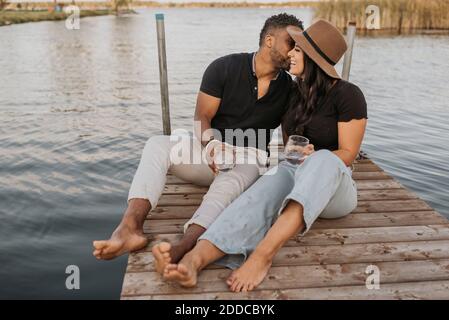 Freund küssen Freundin während sitzen auf Pier gegen See Stockfoto