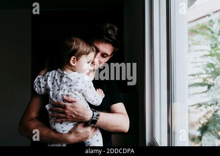 Vater hält Sohn beim Blick durch das Fenster zu Hause Stockfoto