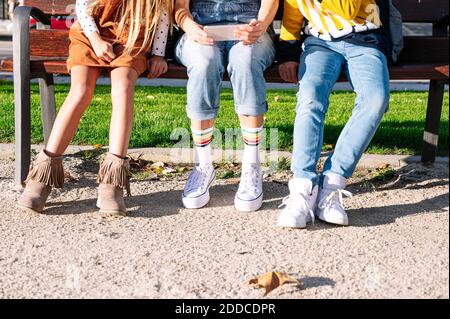 Niedriger Teil der Mutter mit Kindern mit Smartphone sitzen An sonnigen Tagen auf der Bank im öffentlichen Park Stockfoto