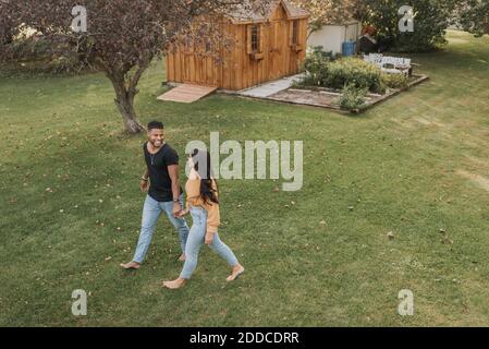 Lächelndes Paar, das die Hände hält, während es im Hinterhof geht Stockfoto