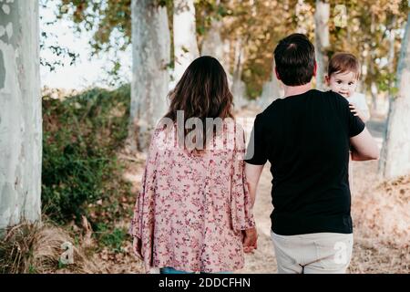 Vater trägt Baby, während die Hand der Mutter im Freien Stockfoto