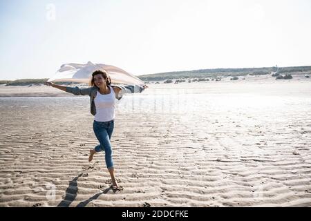 Sorglose Frau läuft, während sie die Decke am Strand bei Sonnenschein hält Tag Stockfoto