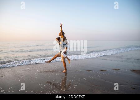 Junger Mann, der der Freundin am Strand Huckepack gab Gegen klaren Himmel bei Sonnenuntergang Stockfoto