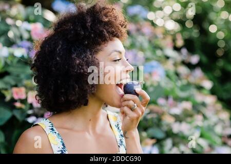 Mittlere Erwachsene Frau, die vor der Blüte steht und figwhile isst Anlage im Park Stockfoto