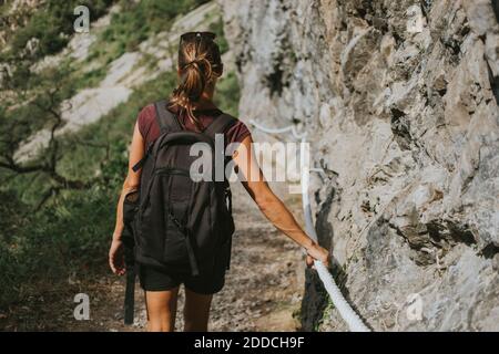 Weibliche Trekkerin mit Rucksack, der sich bergab bewegt, während sie das Seil festhält Felsformation Stockfoto