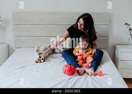 Mutter sitzt mit Sohn weraing halloween Kostüm und Hund liegen Auf dem Bett zu Hause Stockfoto