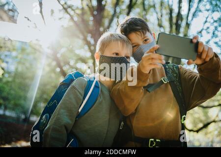 Brüder, die Selfie auf dem Smartphone tragen schützende Gesichtsmaske Stehen im öffentlichen Park Stockfoto