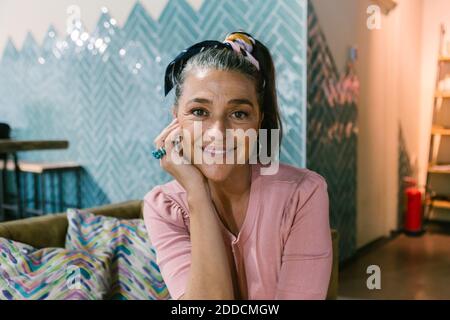 Lächelnde reife Frau, die im Café mit der Hand auf dem Kinn sitzt Stockfoto