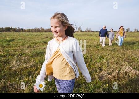 Lächelndes Mädchen, das auf dem Feld läuft, während die Familie im Hintergrund ist Stockfoto