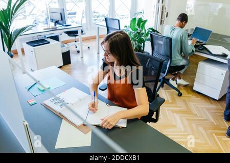 High-Winkel-Ansicht der weiblichen Unternehmerin schriftlich in Tagebuch an Schreibtisch Stockfoto