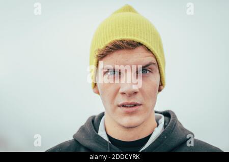 Junger Mann mit Strickmütze, der im Winter gegen die Wand steht Stockfoto