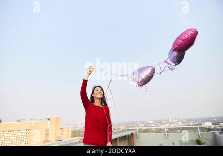 Lächelnde Frau mit einem Ballon in Herzform, der gegen den klaren Himmel steht Stockfoto