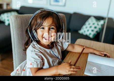 Fröhliches Mädchen trägt Kopfhörer am Schreibtisch Stockfoto