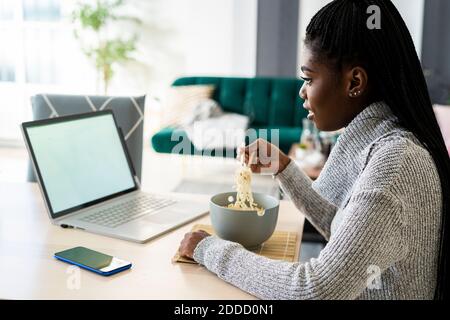 Frau, die Nudeln isst, während sie sich zu Hause einen Film auf dem Laptop ansieht Stockfoto