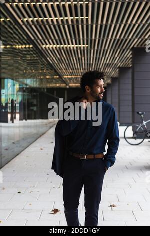 Lächelnder Geschäftsmann hält Blazer beim Spaziergang in der Stadt Stockfoto