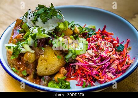 Caponata, wahlweise vegetarisch oder vegan. Mit Aubergine, Zucchini, Cocktailtomate, Zwiebel, Mandeln, Sellerie, Trauben. Wahlweise mit Labneh, einem orientalischen Frischkäse mit Kräutern. In der Mitte eine gebackene Bio-Kartoffeln der Sorte Agria, angebaut in Olching am Stadtrand von München, Deutschland Stockfoto