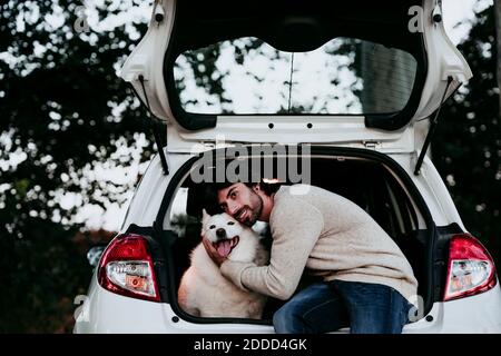 Mann umarmt Hund, während er im Kofferraum am Wald sitzt Stockfoto