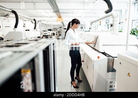 Geschäftsfrau, die Maschinen untersucht, während sie digitale Tablets in der Industrie hält Stockfoto