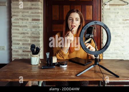 Kosmetikerin Anwendung Lippenstift während Make-up Tutorial auf mobile Telefon zu Hause Stockfoto