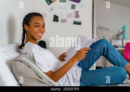 Teenager-Mädchen schreiben im Übungsbuch, während sie auf dem Bett sitzen Zu Hause Stockfoto