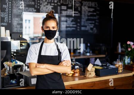 Porträt der Kellnerin in Schutzmaske mit gekreuzten Armen Im Café stehen Stockfoto