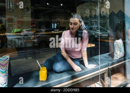 Frau, die beim frischen Saft im Cafe sitzt und durch das Fenster gesehen wird Stockfoto