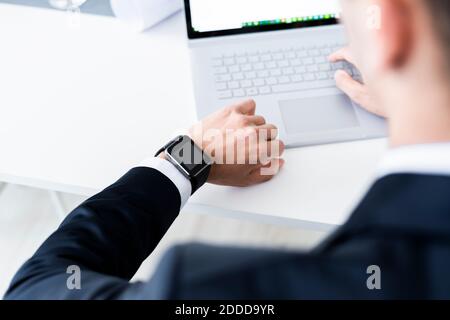 Männliche Unternehmer Überprüfung Zeit, während mit Laptop im Büro Stockfoto