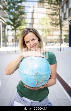 Mittlere Frau hält Globus, während sie auf dem Fußweg in der Stadt steht Stockfoto